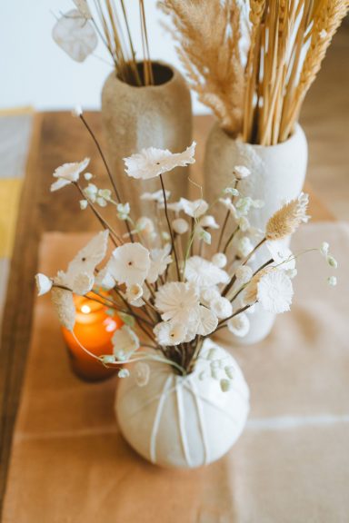 Vases élégants avec des fleurs blanches et une bougie orange sur une table en bois.