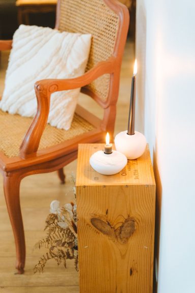 Une chaise en bois, deux bougies sur un support en bois, et un coussin blanc.