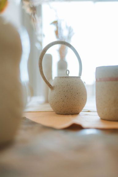 Théière et tasse en céramique sur une table, éclairées par la lumière naturelle.