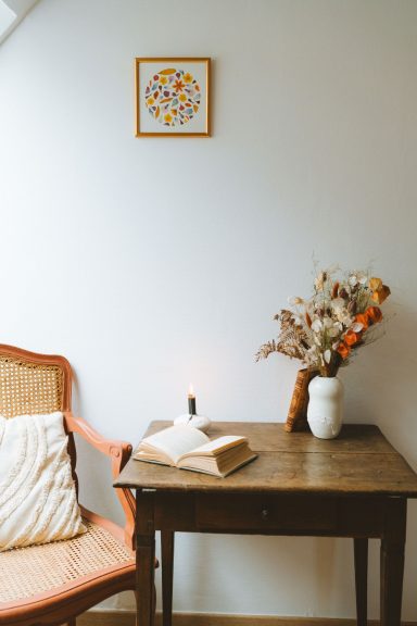 Coin de salon avec une chaise, une table en bois, un vase et un tableau au mur.