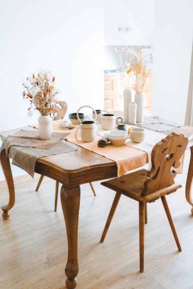 Table en bois avec des décorations, des vases et une chaise dans une pièce lumineuse.