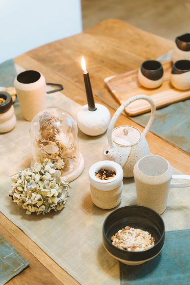 Table décor avec des théières, des tasses, des collations et une bougie allumée.