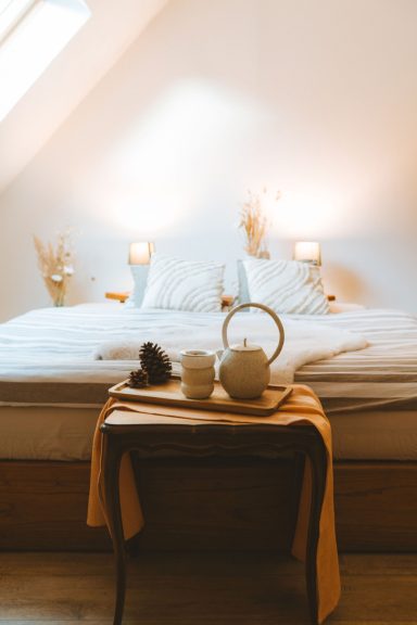 Chambre lumineuse avec lit, lampes, et plateau de thé avec tasses.